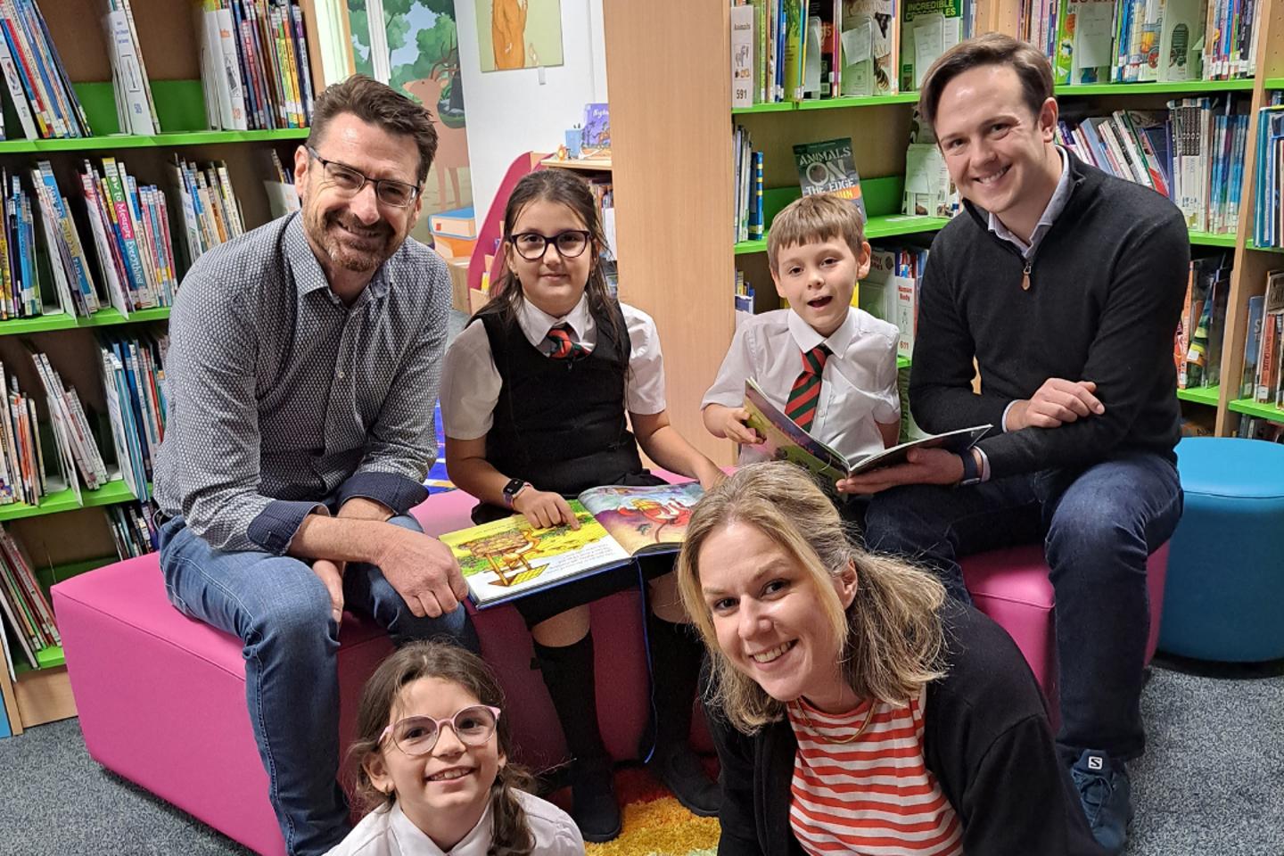 group of adults and school children enjoying storytelling together in a colourful library at Rouge Bouillon School in Jersey.